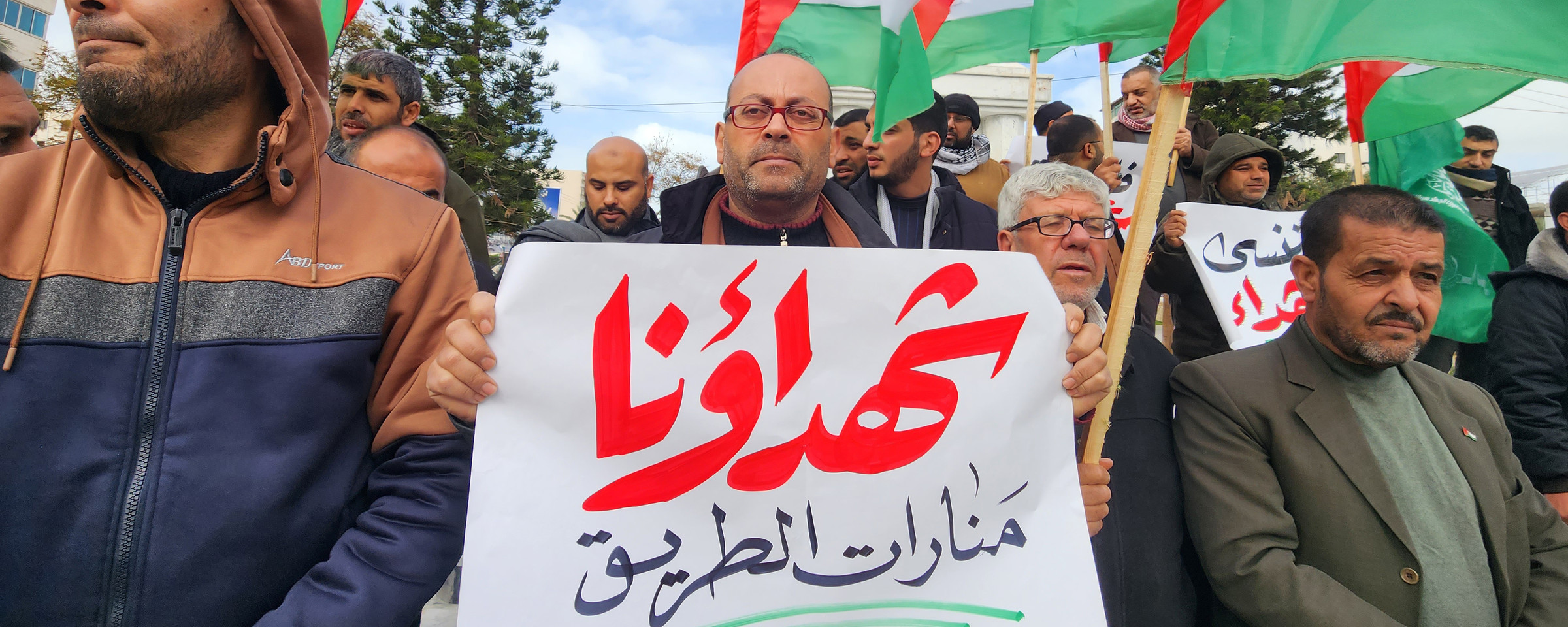 Man holds Arabic-language sign in crowd holding Palestine flags