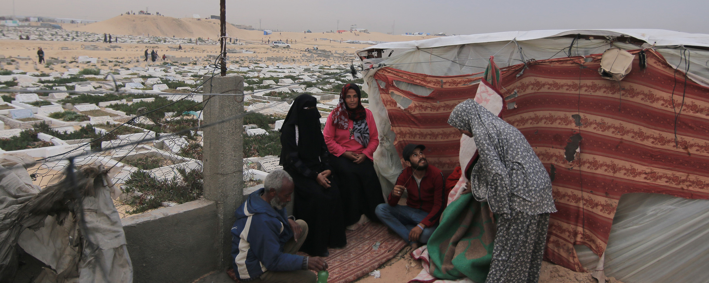 Three women and two men beside a makeshift tent next to a graveyard in Gaza 