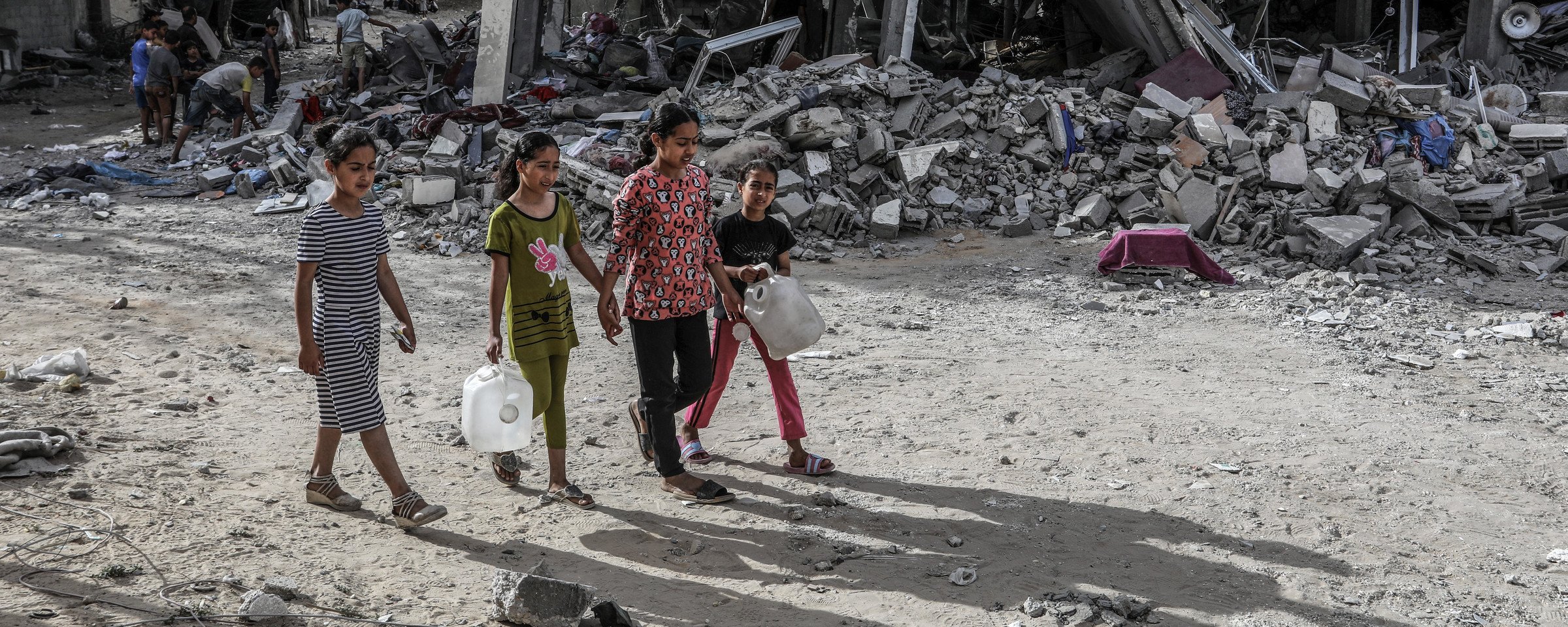 Children carry containers as they walk in front of a building attacked by Israel in southern Gaza 