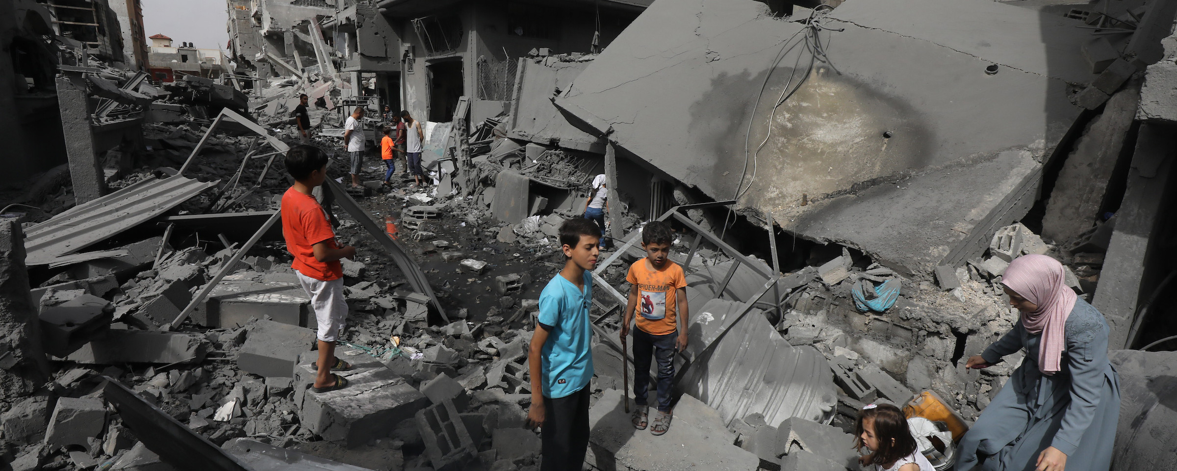 Women and children in brightly colored clothing stand on and walk over concrete rubble