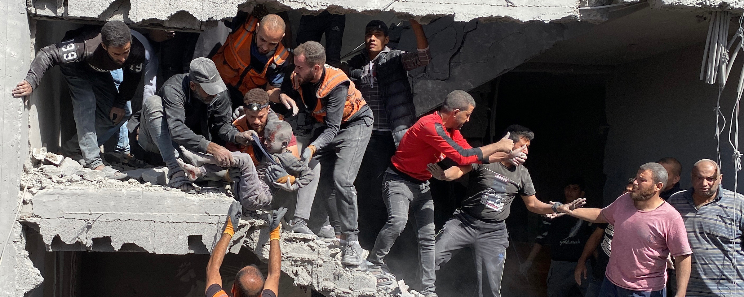 A group of people, some of them wearing orange civil defense vests, work to pull people out of the rubble of a destroyed building