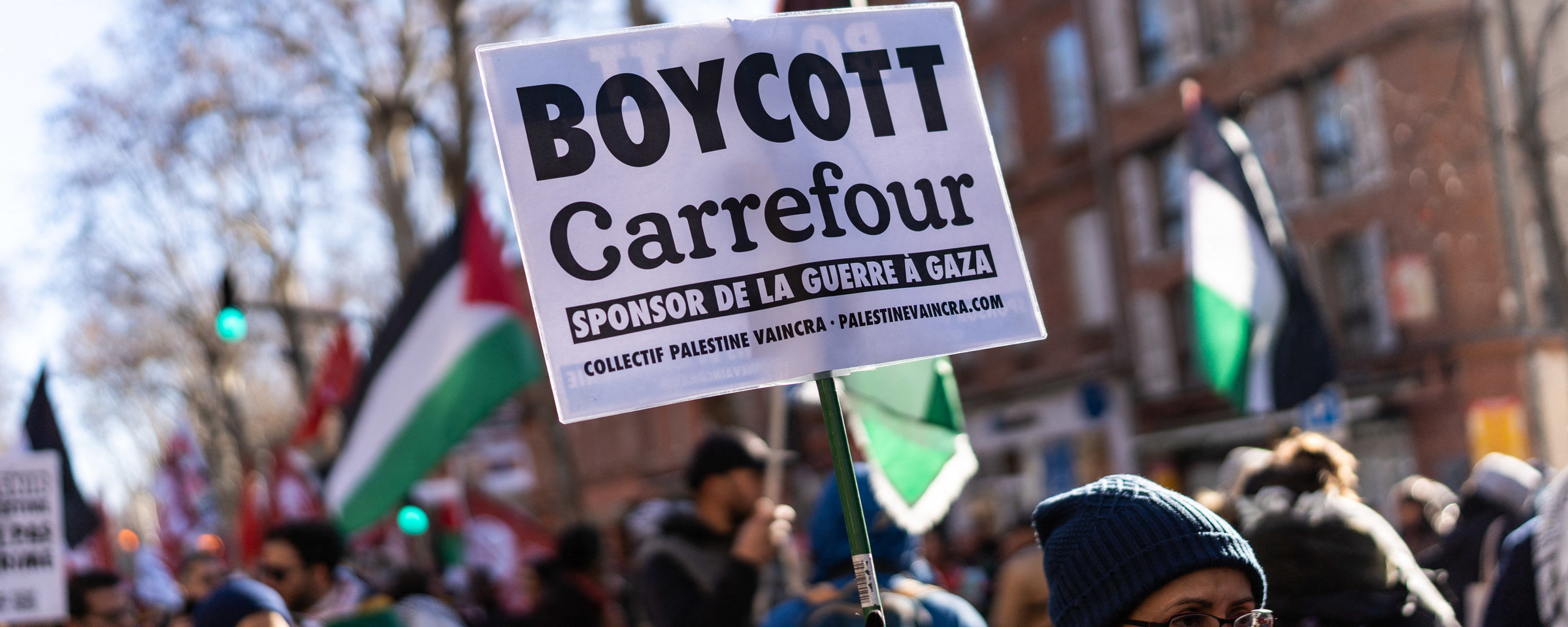 Woman carries sign as others behind her hold Palestinian flags and signs