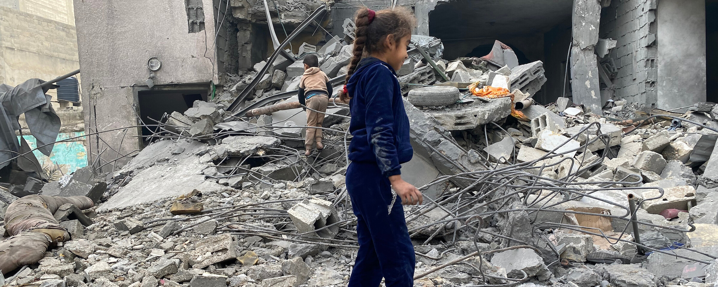 Two young children walk through the rubble of a destroyed house 