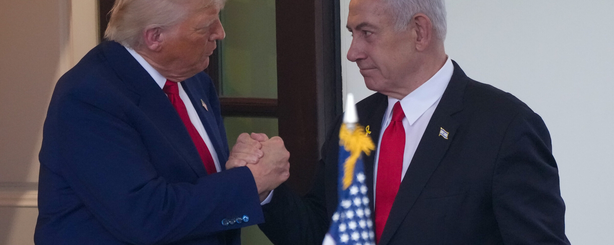 Donald Trump and Benjamin Netanyahu clasp hands behind a US flag