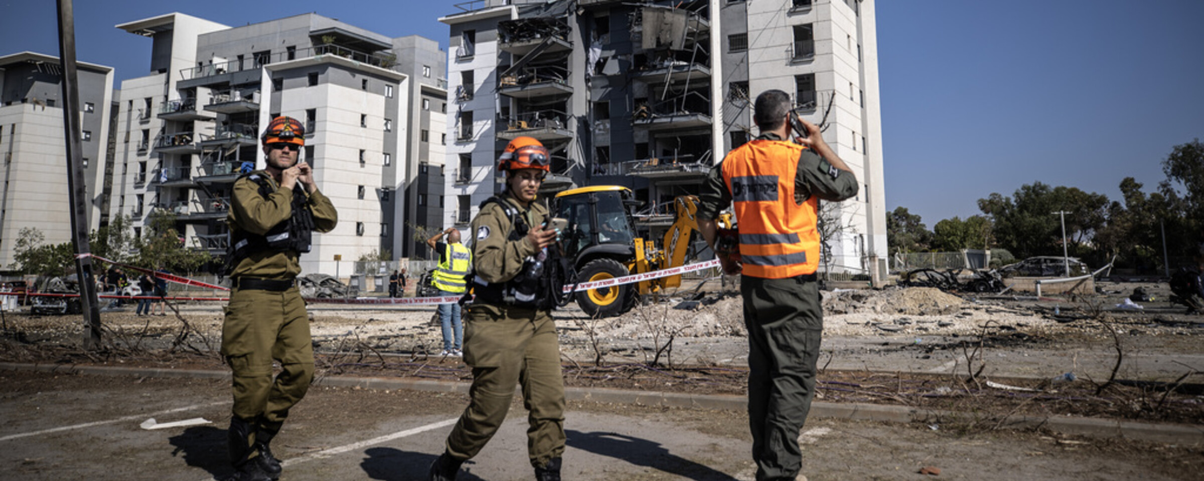 Personnel in uniform stand in front of damaged apartment buildings