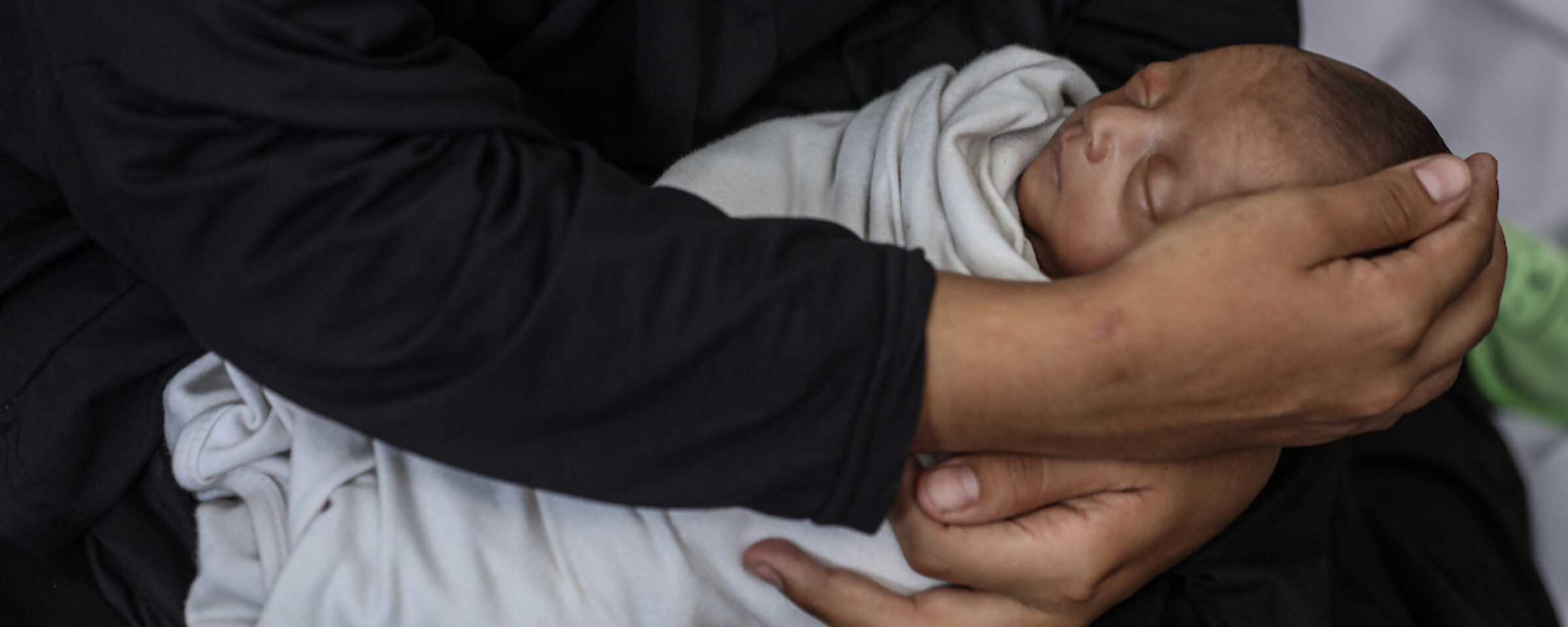 A woman's arms, clothed in black, cradles a sleeping newborn baby wrapped in a white blanket.