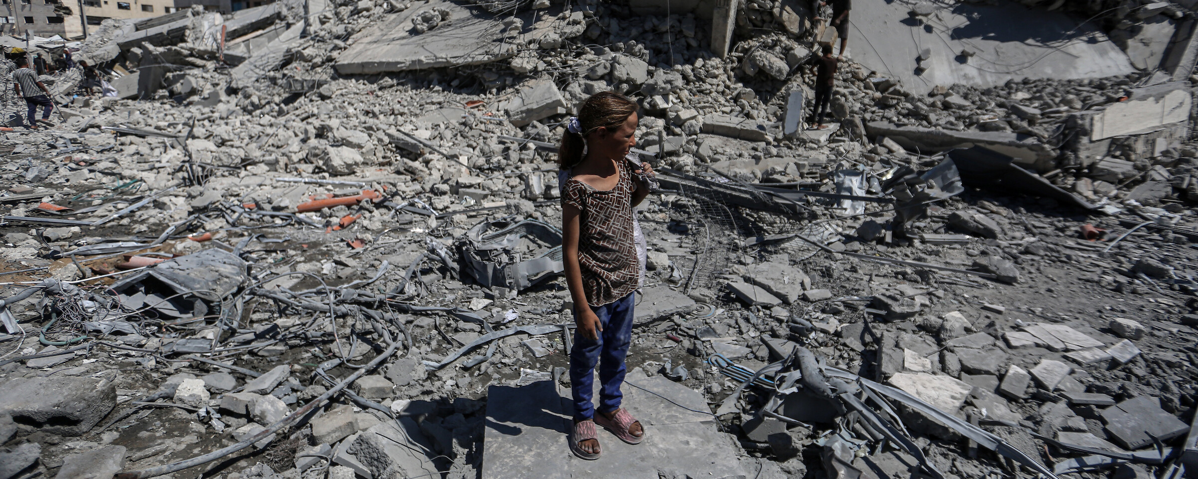 A girl wearing blue pants and a polka dot top stands on a massive pile of concrete rubble.