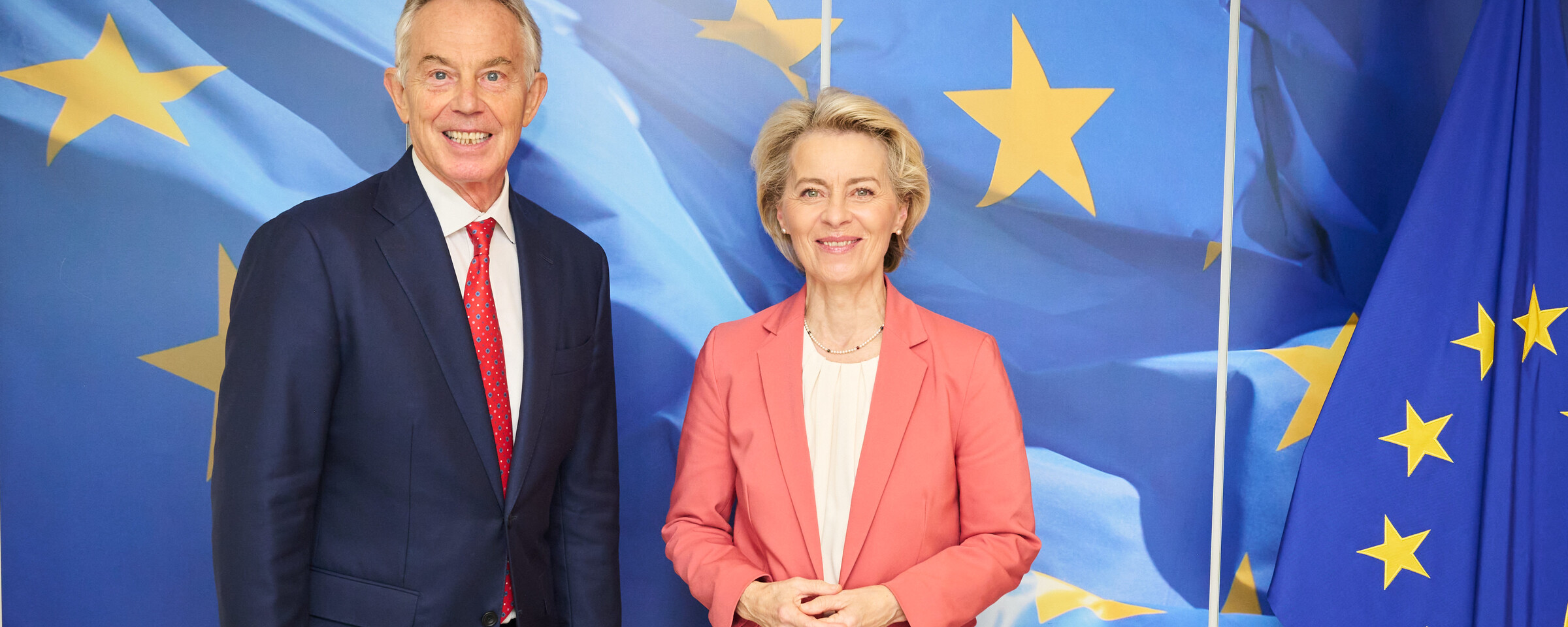 Former British Prime Minister Tony Blair stands beside European Commission President Ursula von der Leyen in front of a blue backdrop featuring yellow stairs