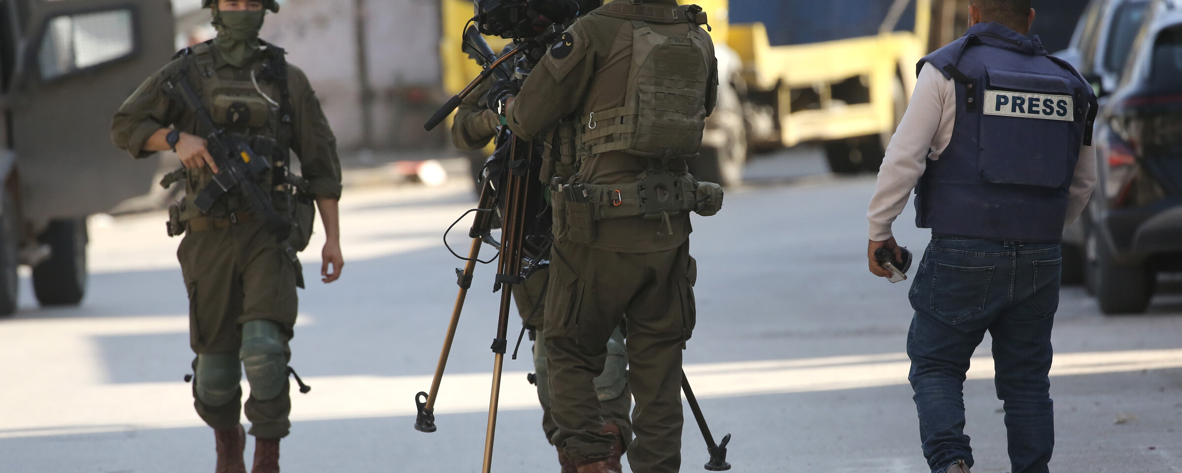 three soldiers surround a camera as a man in press vest looks on
