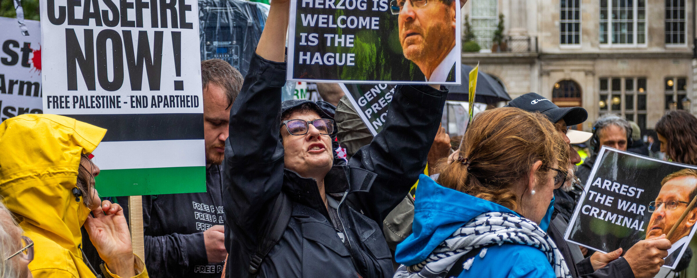 Protesters in London hold up a placard showing a photograph of Israel's President Isaac Herzog beside captions arguing that he should be in The Hague on war crimes charges