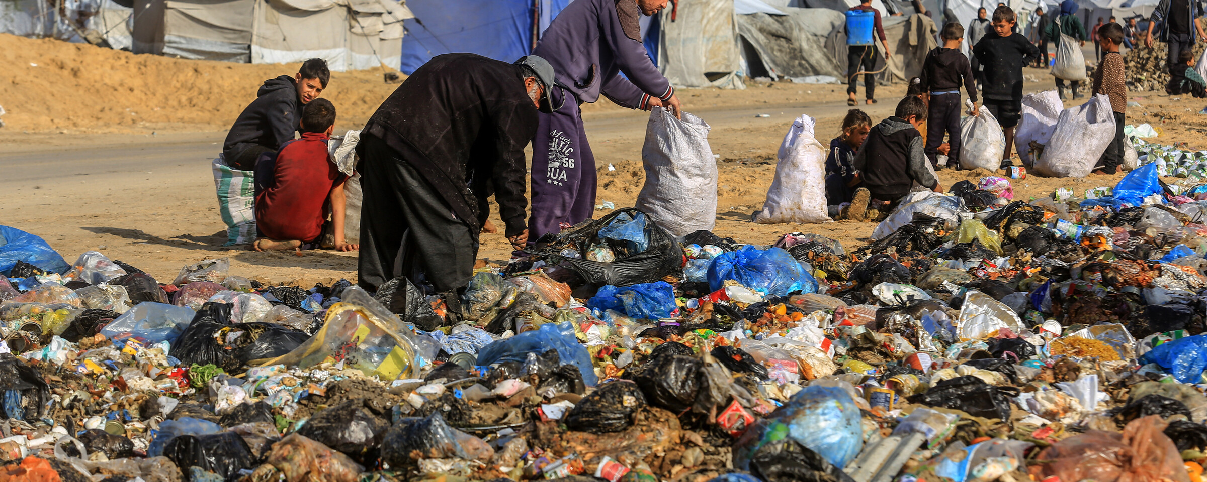 Palestinian adults and children sort through garbage at a landfill north of Khan Younis with tents in the background