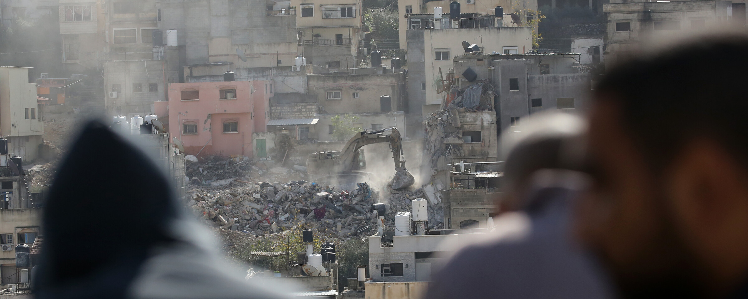 A bulldozer demolishing homes with men watching