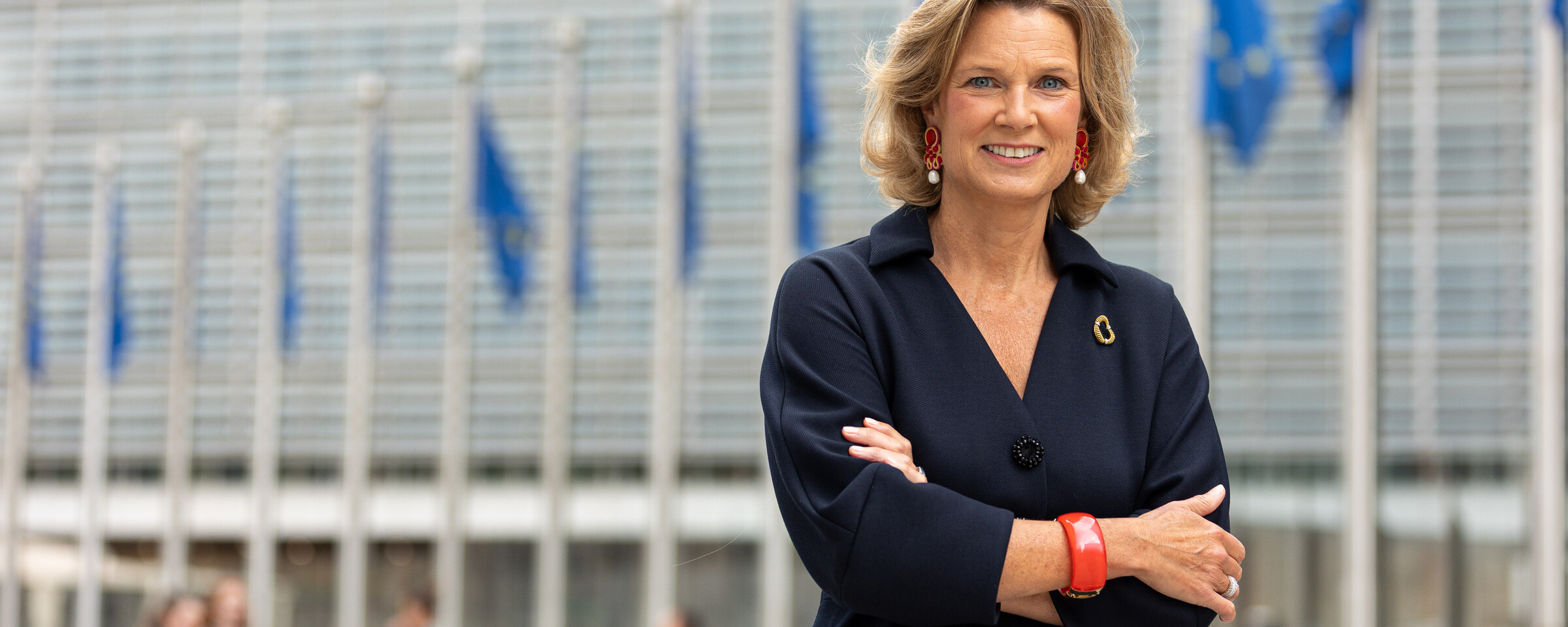 The European Union's Coordinator Against Anti-Semitism Katharina von Schnurbein stands with her arms folded outside a building with poles to which blue and yellow flags are attached 