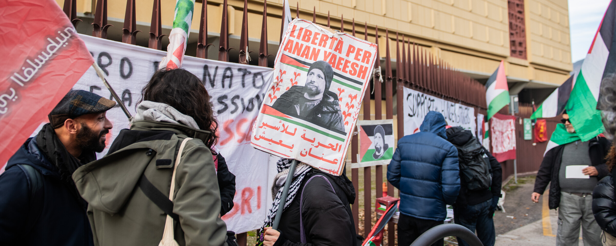 A protester holds a placard reading Liberta per Anan Yaeesh as a number of other people stand beside the protester 