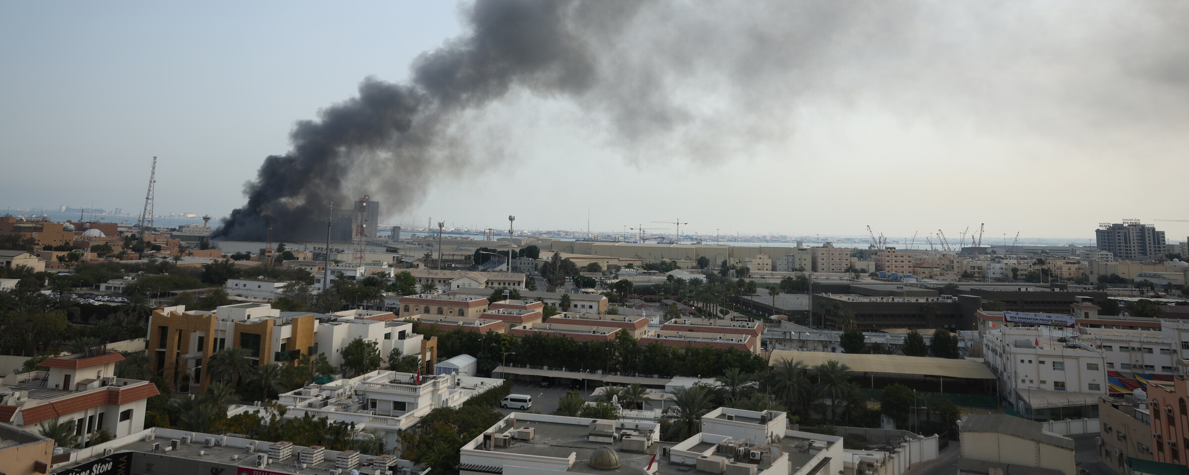A wide urban landscape with thick smoke rising from a large building