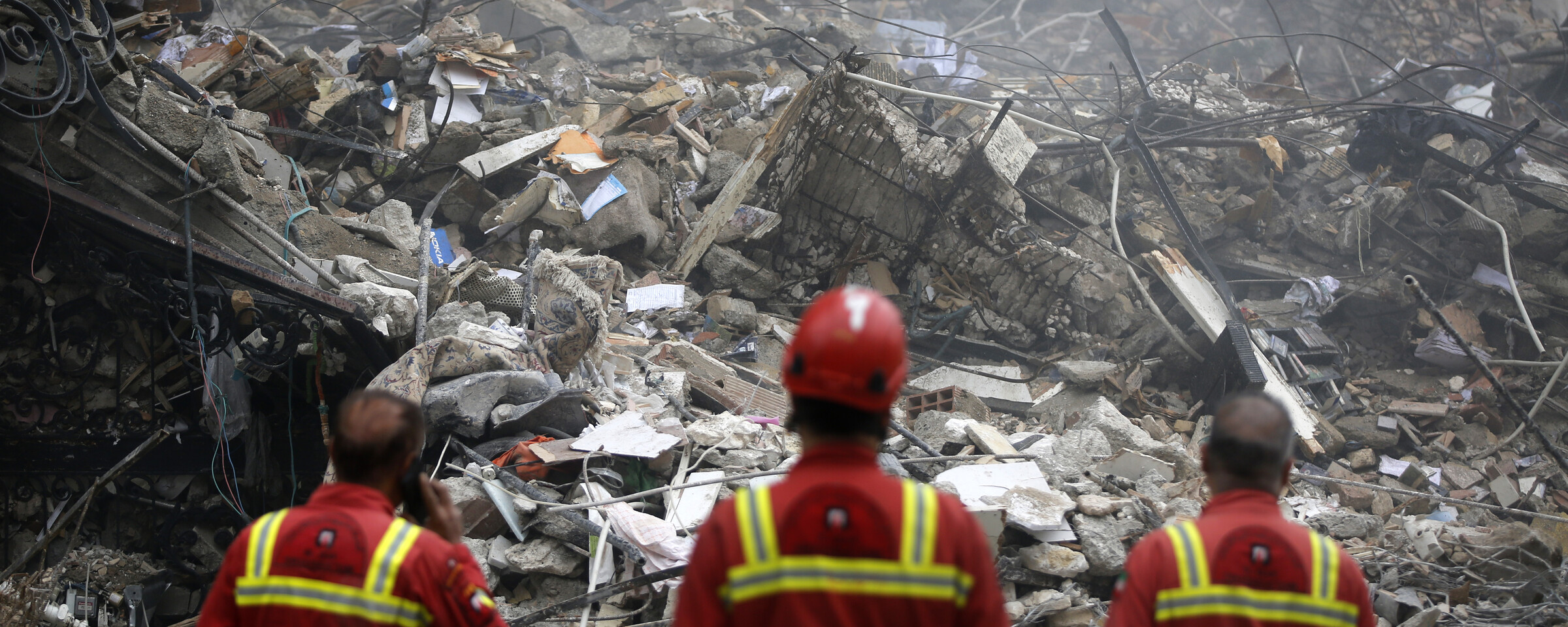 Three first responders stand in front of badly damaged building.