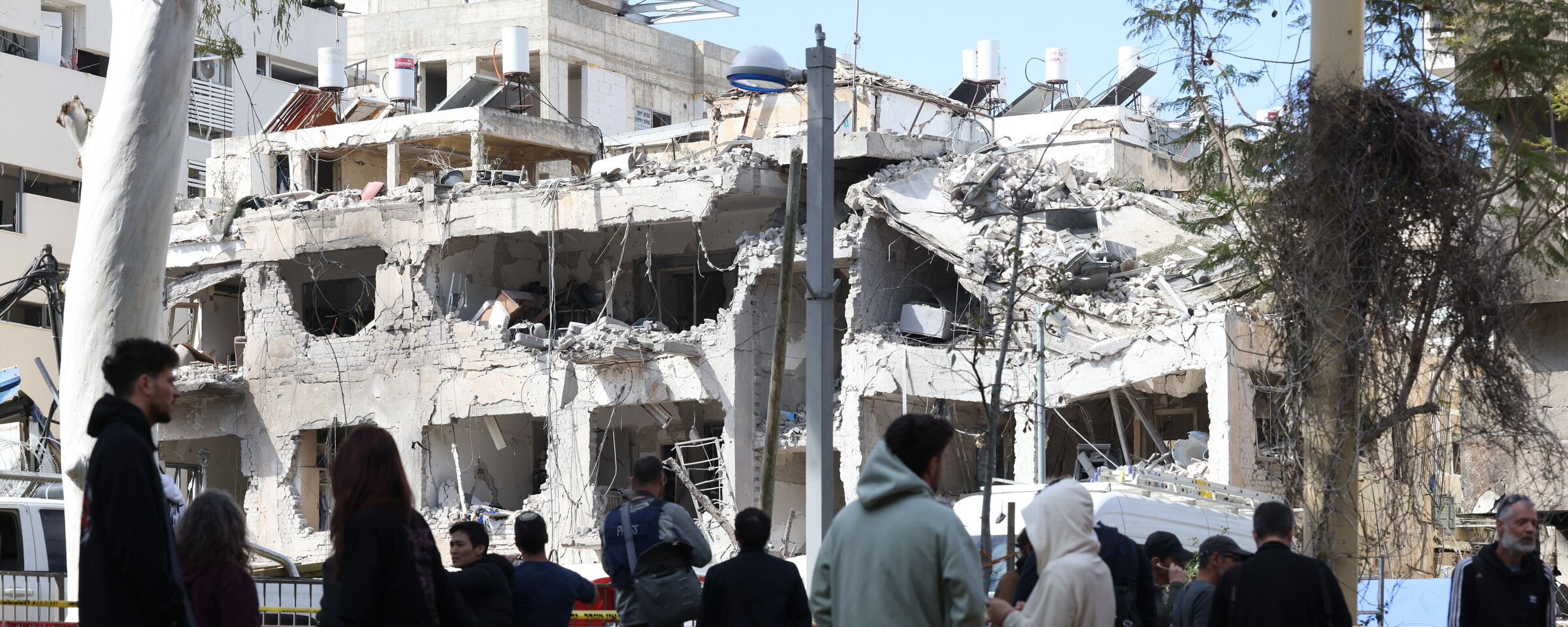 A crowd of people looks up at a partially collapsed apartment building
