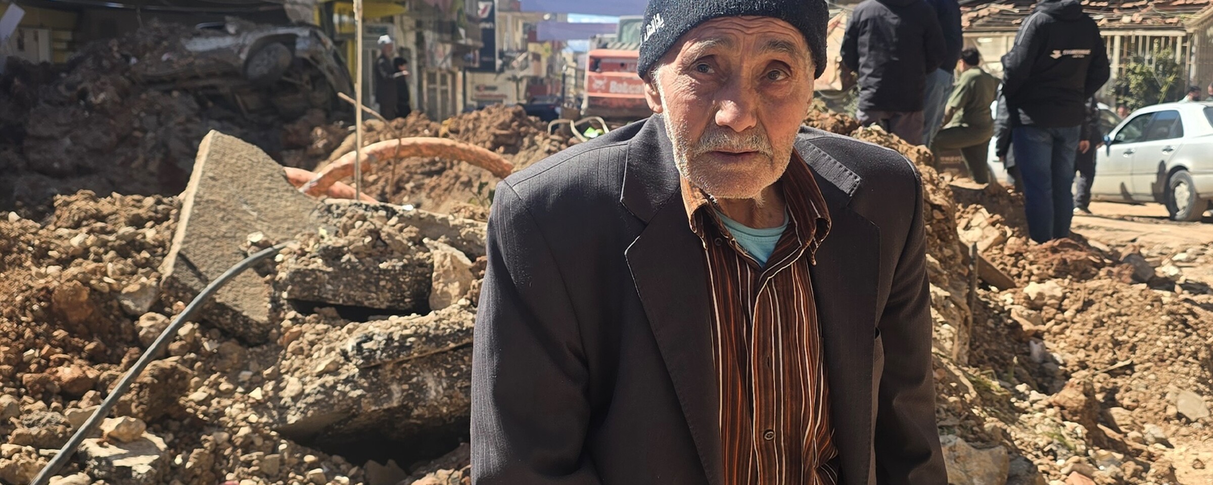 Older man sits in front of rubble of a bombed building