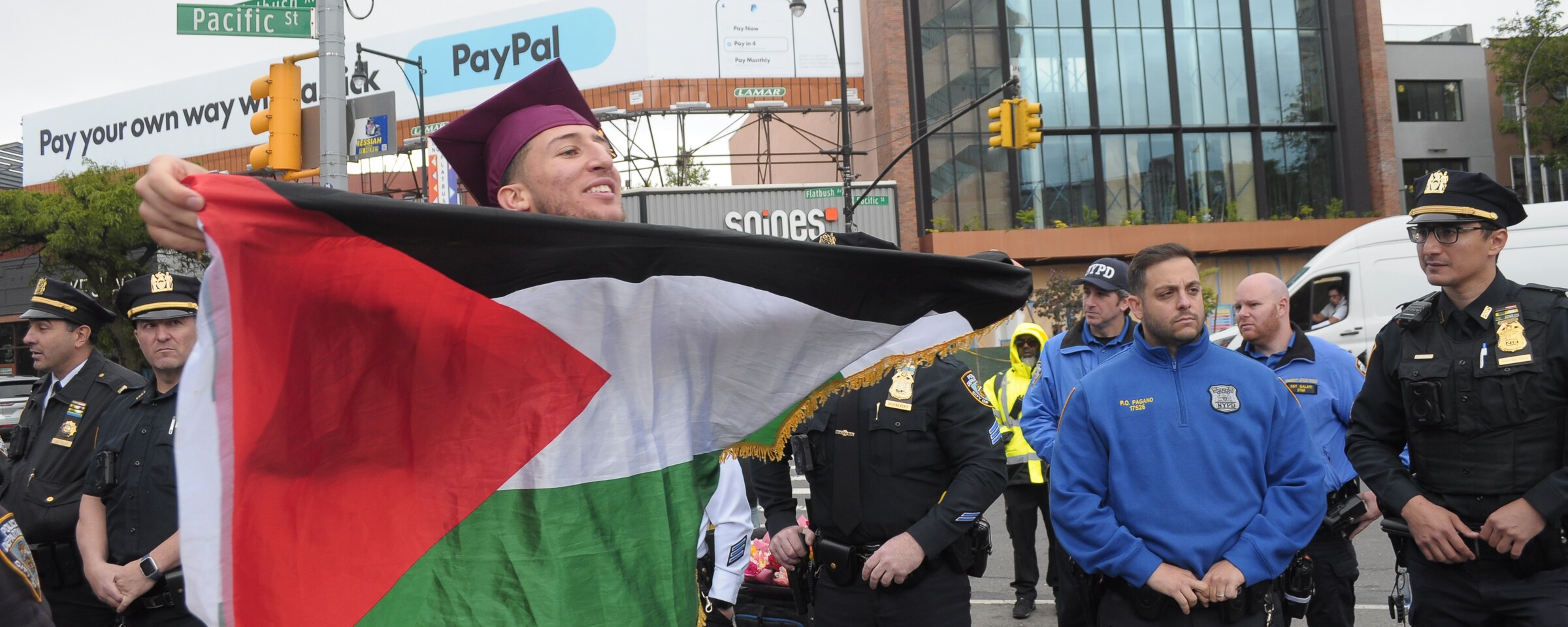 A graduating student with a Palestinian flag protests in New York City as police look on