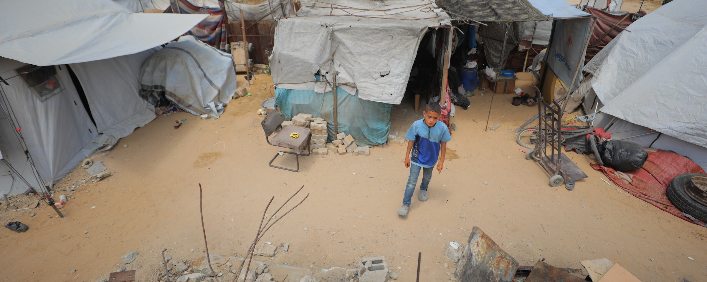 A boy stands in front of a group of tent shelters