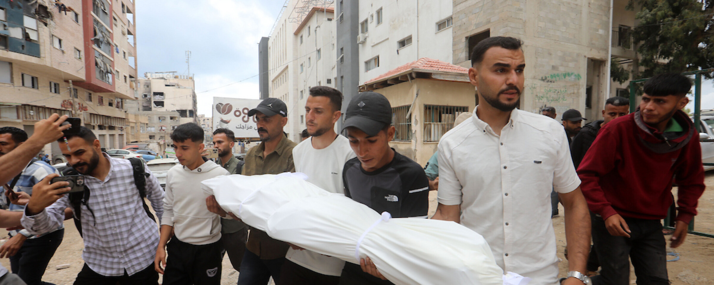 A group of men carry a small body wrapped in a white shroud.