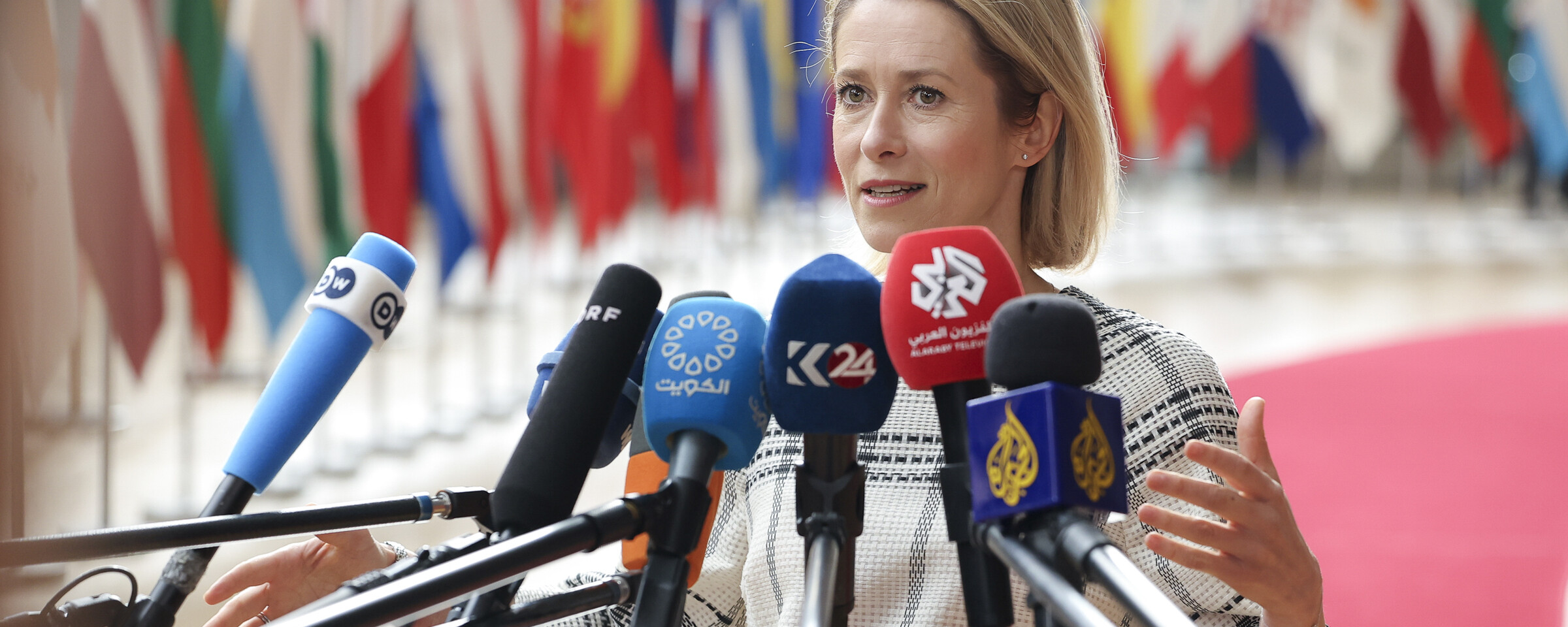 European Union representative Kaja Kallas stretches out her arms as she stands behind several microphones of television channels 