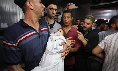 A man surrounded by other people carries the shrouded body of a child