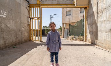 A girl stands before a yellow metal gate