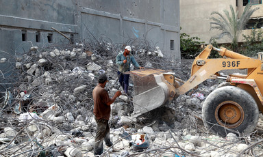 Two Palestinian laborers standing on a pile of rubble, next to a bulldozer
