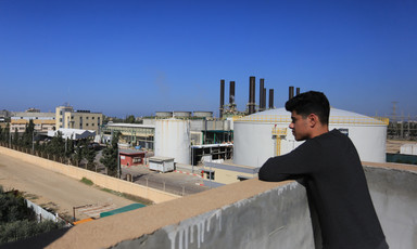 Man stands beside a wall that overlooks a power plant 