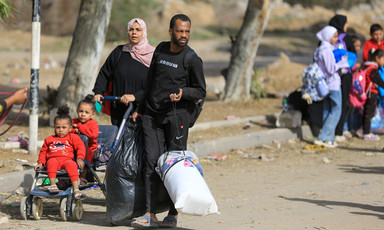 A woman pushes two girls in a pushchair as a man walks beside them carrying bags in Gaza