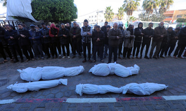 A group of mourners pray over four bodies wrapped in white body bags