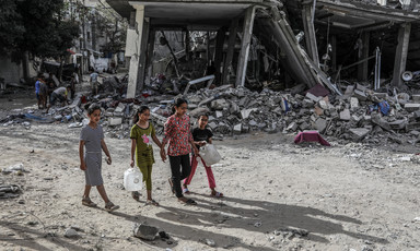 Children carry containers as they walk in front of a building attacked by Israel in southern Gaza 