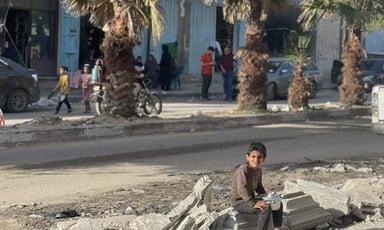 A boy sits on the side of the road, holding a pot. 