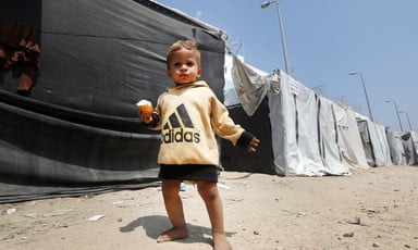 A child stands next to a row of makeshift tents 