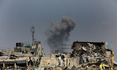 A plume of smoke from an Israeli airstrike rises from a horizon of destroyed buildings