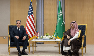 Two men sit flanked by the American and Saudi Arabian flags