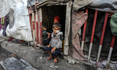 A child and his mother look from the doorway of their tent