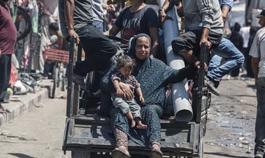 A woman and a child sit on the back of a cart pulled by a donkey