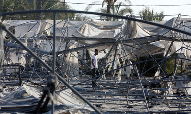 A man walks through the remains of burnt out tents