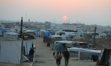 At sunset, people walk between tents in the low light.