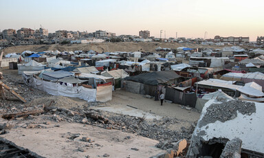 Rows of makeshift tents beside a sand dunes and buildings in southern Gaza 