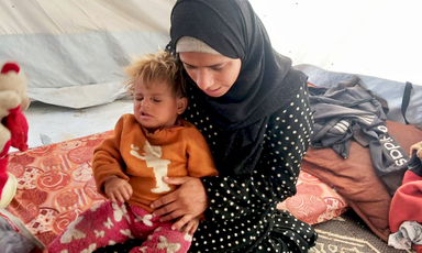 A woman holds her small child on her lap in a tent. 