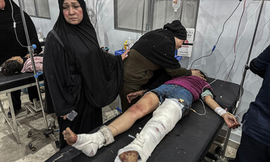 Woman with sad expression stands next to injured girl on stretcher in hospital