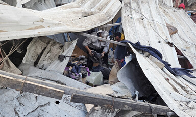 Men sort through personal belongings in a destroyed makeshift shelter