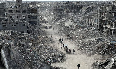 Landscape view shows people walking along cleared road in between collapsed multi-story buildings