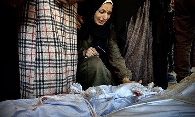 A kneeling woman cries while reaching towards a shrouded body on the ground