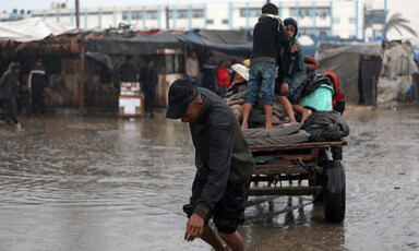 A bare-footed man wearing a baseball cap pulls a loaded cart carrying multiple children