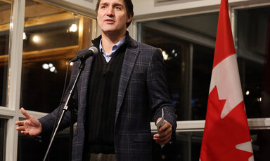 Canadian Prime Minister Justin Trudeau stands behind a microphone and in front of a Canadian flag 