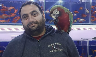 A man poses a red and green parrot on his shoulder